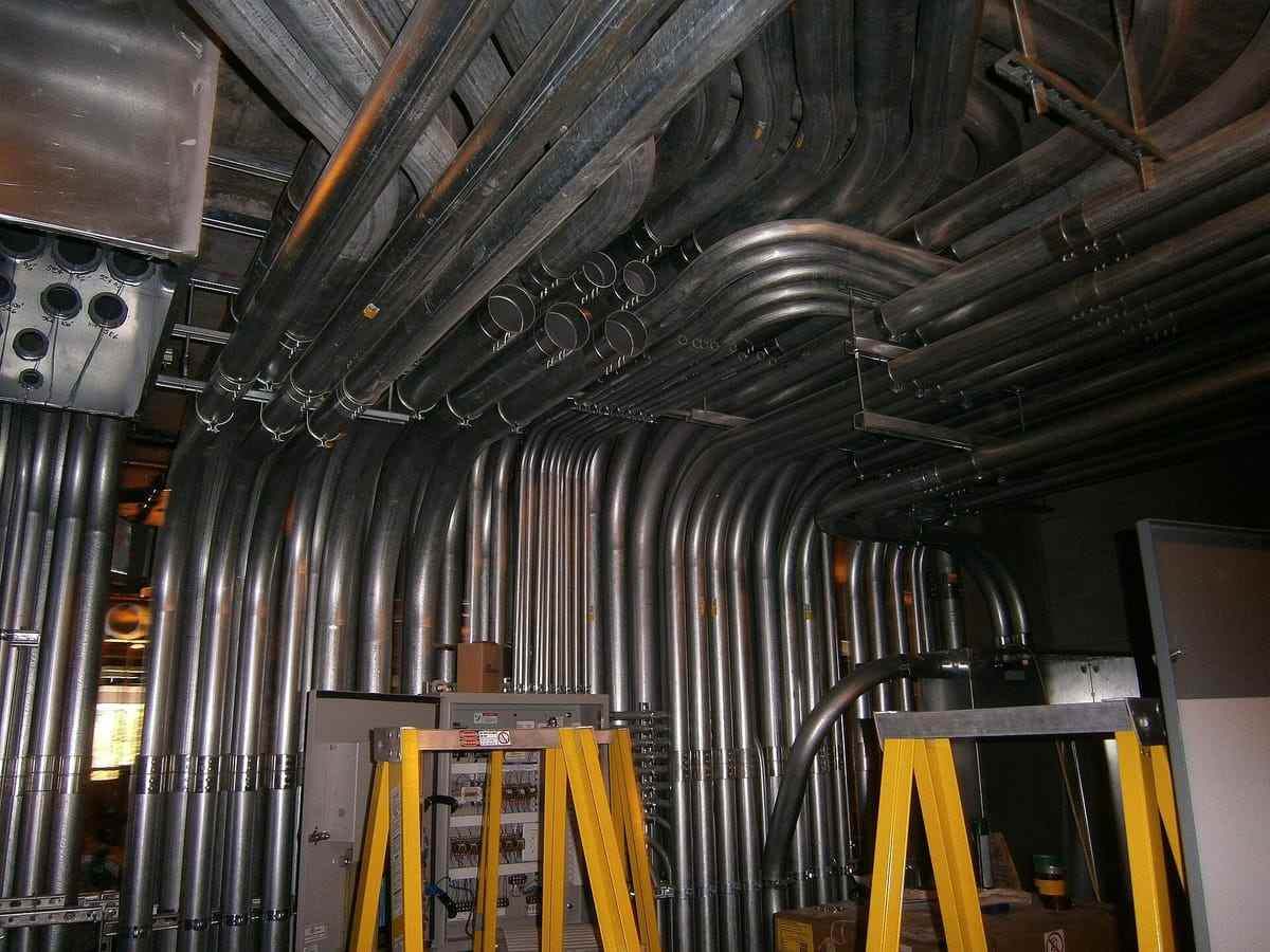 Rows of galvanised conduit run along a plant ceiling above yellow stepladders