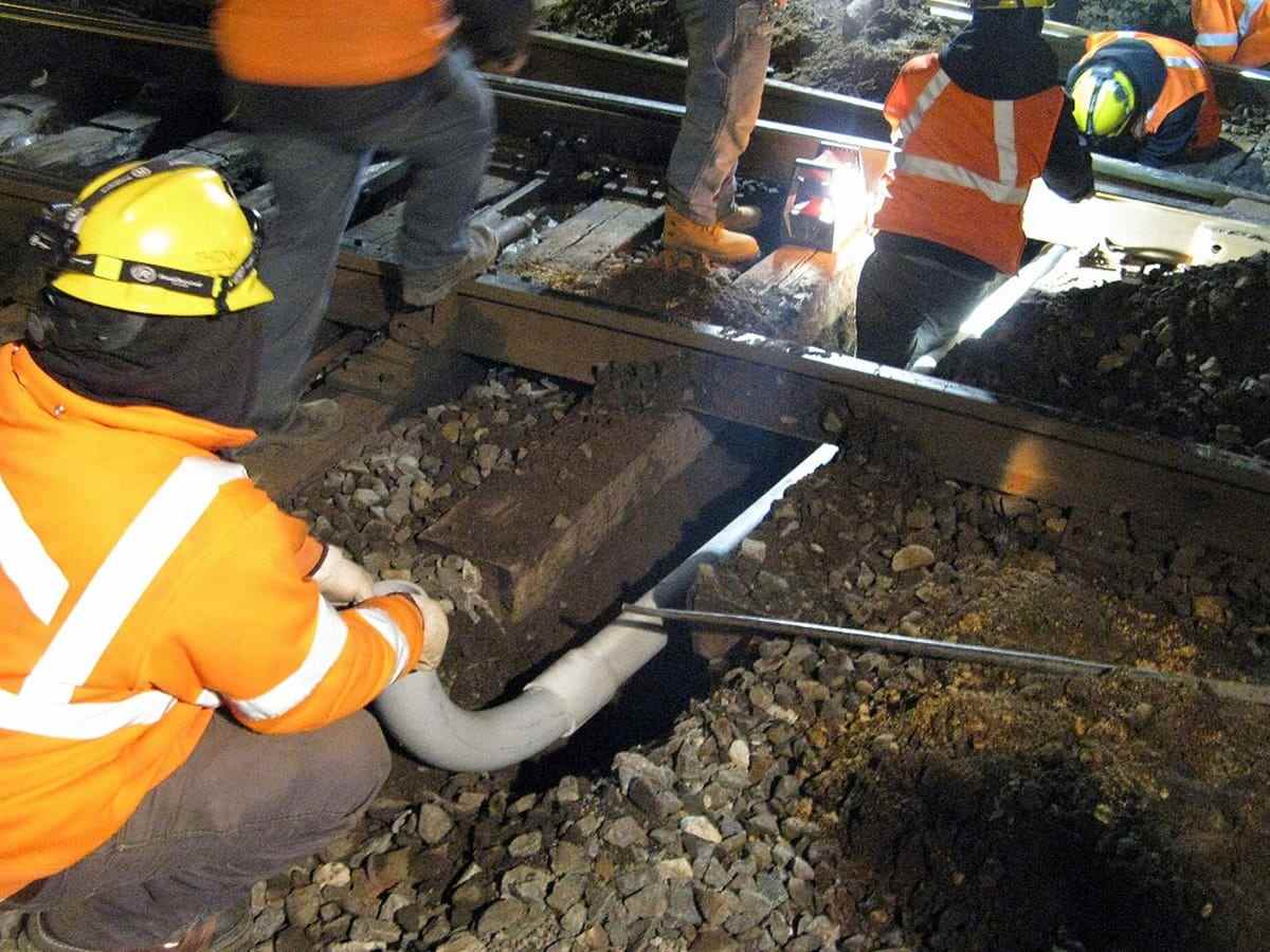 A night crew laying conduit in an excavated trench under work lights