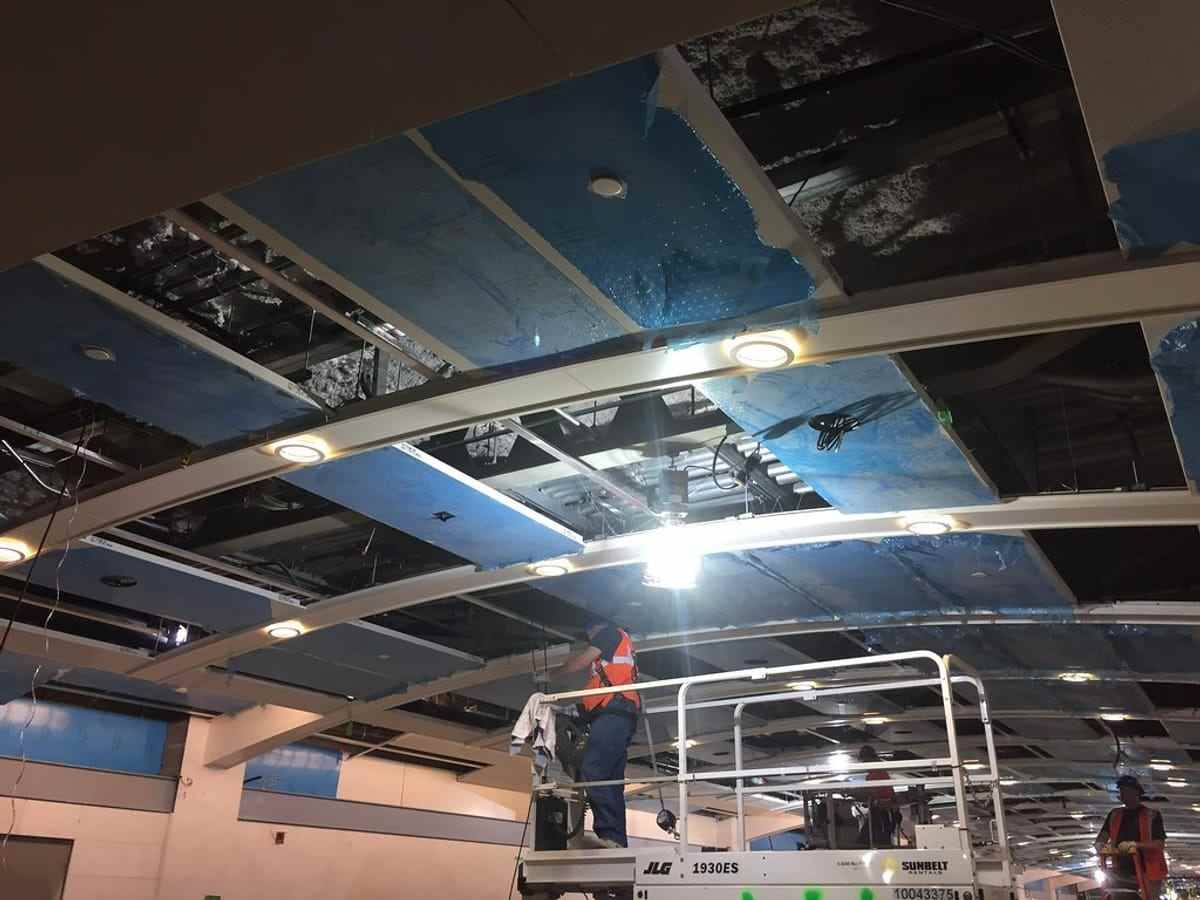 Two electricians pulling cable through overhead conduit in a new concourse