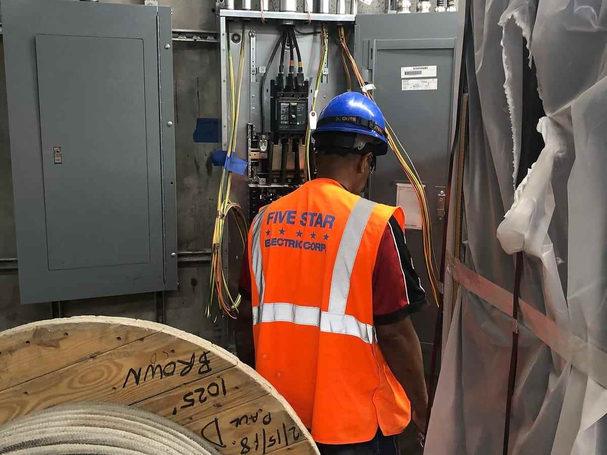 An electrician in hi-vis terminating branch circuit wiring inside a panel